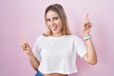 Young blonde woman standing over pink background smiling confident pointing with fingers to different directions. copy space for advertisement 