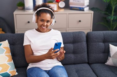 Afro-Amerikalı kadın evdeki kanepede oturmuş müzik dinliyor.