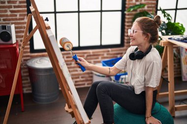 Sanat stüdyosunda paten boyasıyla resim çizen genç sarışın kadın sanatçı.
