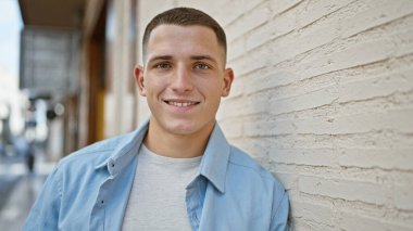 Yakışıklı bir İspanyol genç, güneşli bir şehir sokağında kendinden emin bir şekilde gülümsüyor..