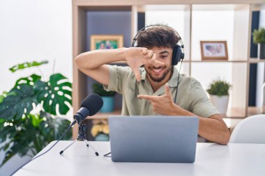 Radyoda çalışan sakallı bir Arap gülümseyerek elleri ve parmakları gülen yüzlü bir çerçeve yapıyor. yaratıcılık ve fotoğrafçılık kavramı. 