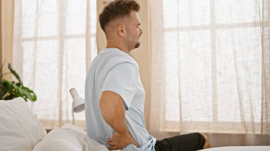 Sakallı genç İspanyol bir adam evdeki yatak odasında sırt ağrısı çekiyor.