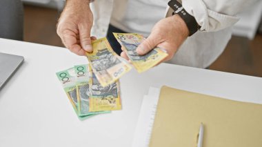 Yakışıklı, orta yaşlı beyaz iş adamı. Ofiste yığınla Avustralya doları sayıyor. Yatırım başarısı elde ediyor.