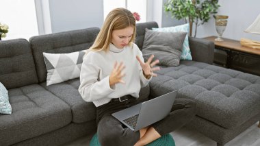 Modern oturma odasında dizüstü bilgisayar kullanan sinirli bir kadın.