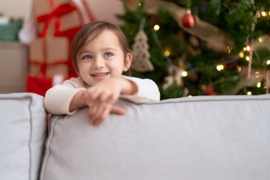 Evdeki Noel ağacının yanında duran tatlı kız kanepeye yaslanıyor.