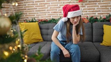 Genç, güzel, İspanyol bir kadın Noel 'i kutluyor. Kanepede oturmuş, eve üzgün üzgün bakıyor.