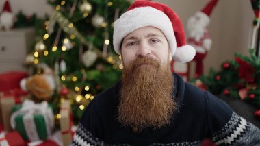 Genç kızıl saçlı adam Noel ağacının yanında oturuyor.