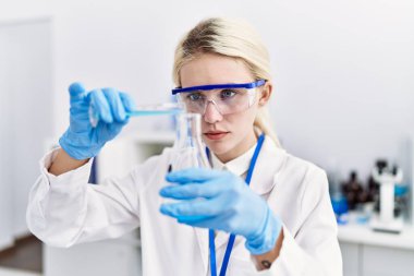 Laboratuvarda test tüpüne sıvı döken genç sarışın bilim kadını.