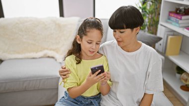 Mutlu anne ve kız evdeki rahat bir kanepede birlikte oturup eğlenirken akıllı telefon mesajlarının keyfini çıkarıyorlar, evde rahat bir yaşam tarzının ortasında pozitif neşe yayıyorlar.