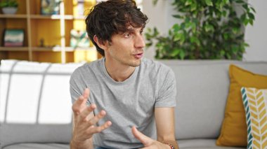 Genç İspanyol bir adam yan koltuğa oturmuş evde konuşuyor.