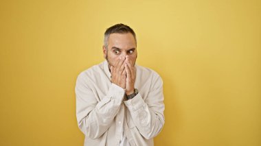 Gri sakallı olgun bir İspanyol, sarı duvarlı arka planda sürpriz yapıyor..