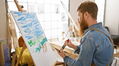 Yakışıklı, odaklı genç adam yaratıcılığını kanalize ediyor, stüdyoda resim çiziyor, elinde fırça var..