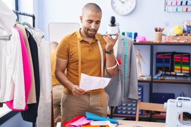 Genç Latin terzi atölyedeki akıllı telefondan konuşuyor.