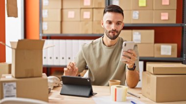 Ofisteki dokunmatik ve akıllı telefonları kullanan Latin asıllı genç bir adam.