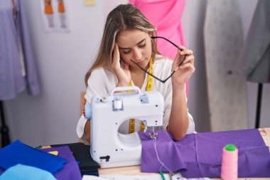 Young blonde woman tailor stressed using sewing machine at clothing shop