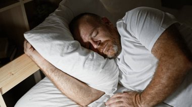 Handsome middle-aged caucasian man, comfortably resting in the cozy atmosphere of his bedroom, peacefully asleep engulfed in the soft morning light. clipart