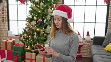 Kafkasyalı genç bir kadın akıllı telefon kullanarak Noel 'i evde kutluyor.