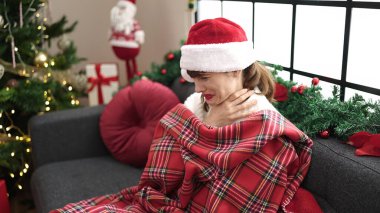 Young caucasian woman feeling sick and cold sitting on the sofa at christmas at home clipart