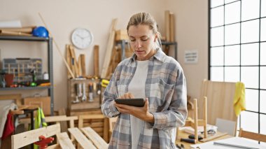 Parlak, düzenli bir marangozluk atölyesinde tablet kullanan odaklanmış genç bir kadın..