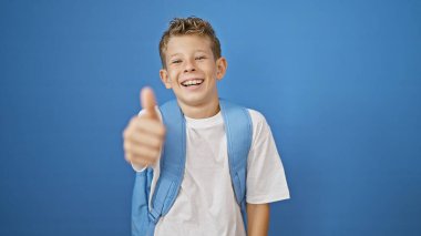Sevimli, sarışın bir çocuk mavi izole bir arka plana karşı duruyor, gülümserken kendine güvenen bir baş parmak hareketi yapıyor. Küçük, mutlu, zeki bir çocuk çalışmaktan zevk alıyor.!