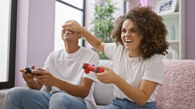 Neşeli bir çift, elleri kapalı, evdeki kanepede oyun oynuyorlar.