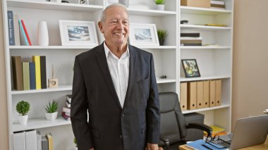 Kendinden emin ve gülümseyen kıdemli bir adam iş büyüsü yapıyor. Ofiste başarılı olurken etrafa neşe saçıyor.