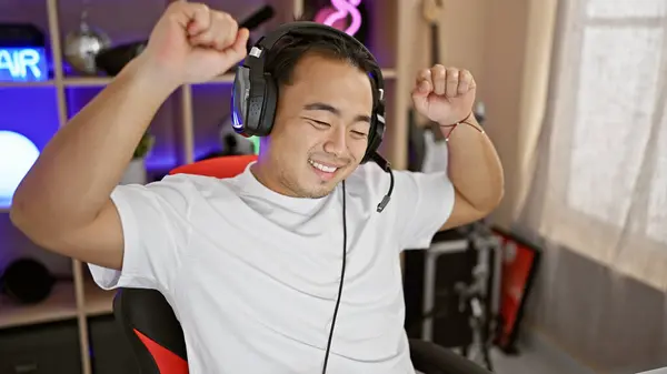 Vibrant young chinese gaming streamer, confidently dancing and smiling in his indoor gaming room at night, streaming live and bringing on the entertainment!
