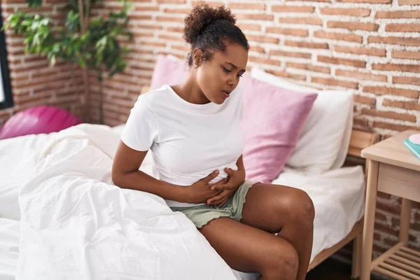 African american woman suffering for menstrual pain sitting on bed at bedroom