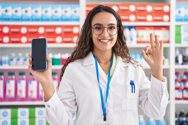 Mladá Hispánská Žena Pracující Lékárně Která Ukazuje Obrazovku Smartphonu Usmívá — Stock fotografie