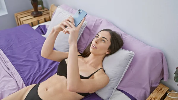 Молодая Красивая Латиноамериканка Лежит Кровати Выглядит Сексуально Используя Смартфон Спальне — стоковое фото