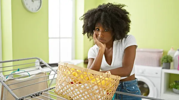 アフリカ系アメリカ人女性が洗濯室で疲れた服でバスケットに乗る — ストック写真