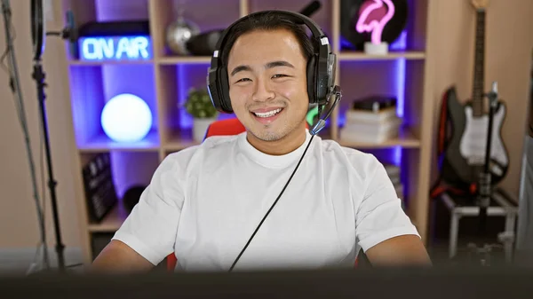 Confident young chinese man, a digital gamer streamer, smiling with headset in dark gaming room, mastering futuristic cyber entertainment while streaming