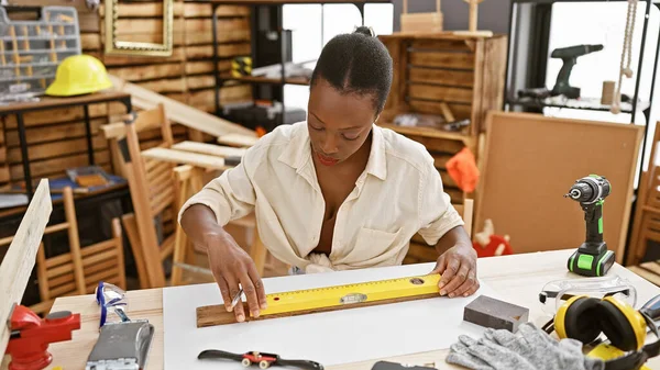 Beautiful african american woman carpenter measuring wood plank, a glimpse into carpentry and construction industry