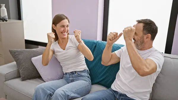 Father and daughter sharing a fun-filled celebration at home, sitting together on the sofa, watching television with happy smiles