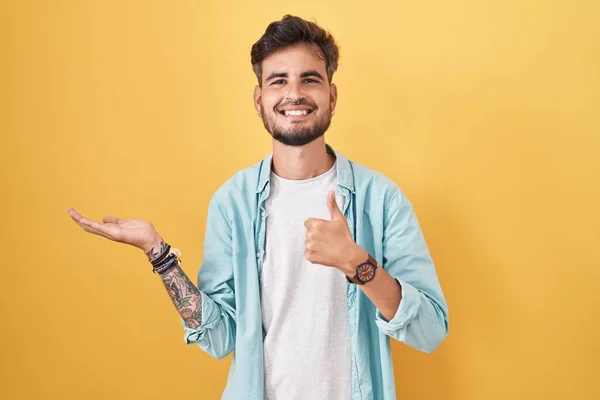 Young Hispanic Man Tattoos Standing Yellow Background Showing Palm Hand — Stok fotoğraf