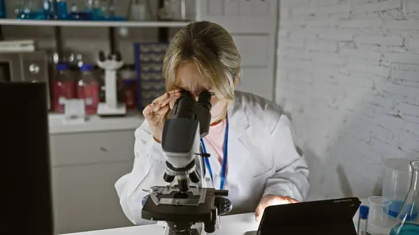 stock image A caucasian woman scientist meticulously analyzes a sample through a microscope in a well-equipped laboratory indoors.