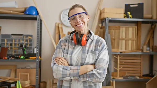 在一个精心组织的木工车间里 身穿安全护目镜 戴着护目镜 头戴护目镜 有自信的年轻女子交叉双臂 — 图库照片