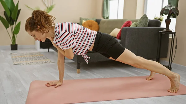A fit woman performs a plank exercise on a pink mat in a cozy living room, depicting a healthy lifestyle.