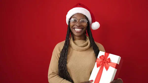 非洲女人带着自信的笑容 带着圣诞礼物 远离孤独的红色背景 — 图库照片