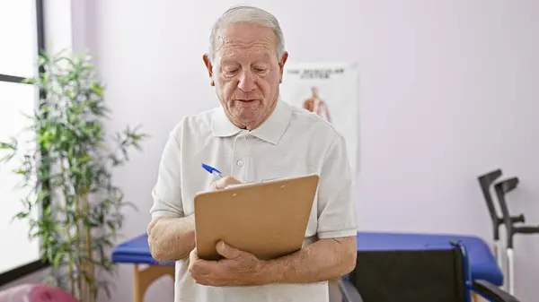 Dedicated elder man physio therapist diligently taking notes at bustling rehab clinic, providing unmatched kinesiology and chiropractic treatments to senior patients