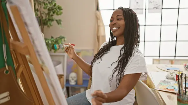 Smiling african american woman painting on a canvas in a bright art studio