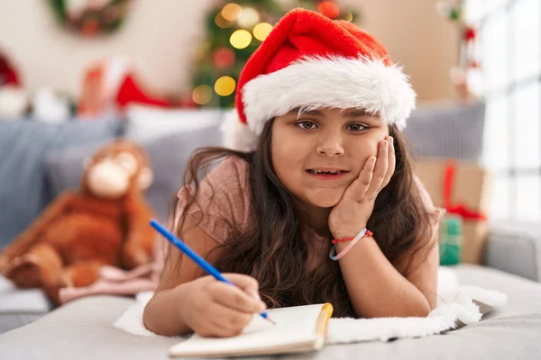 他的惊慌失措的女儿躺在沙发上写在家里的圣诞树旁 — 图库照片