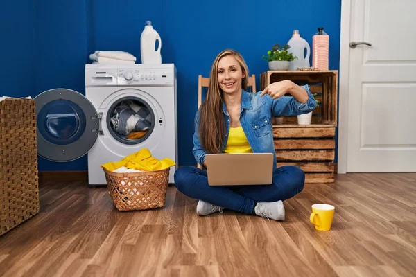 Young Blonde Woman Doing Laundry Using Laptop Pointing Finger One — Stock Photo, Image