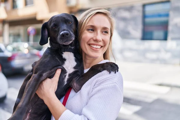 Young blonde woman smiling confident hugging dog at street