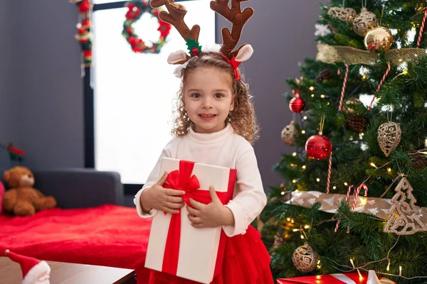 Sevimli sarışın kız Noel ağacının yanında hediyesini kucaklıyor.