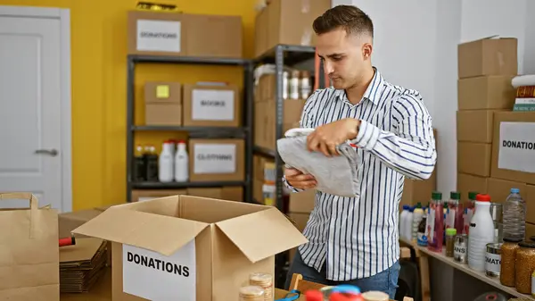 Handsome young hispanic man organizing donations in a storehouse with cardboard boxes and supplies in the background.