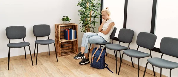 Young blonde woman sitting on chair looking upset at waiting room
