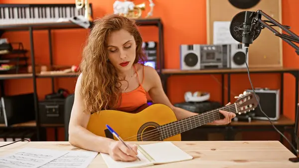 Caucasian woman songwriting with guitar in a music studio