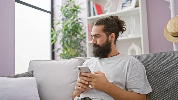 Bearded Young Man Lounges Grey Couch Home Absorbed His Smartphone — Stock Photo, Image