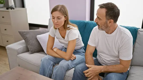 Unhappy father and daughter locked in a heated argument while sitting on the sofa at home, their love stretched thin amid this family disagreement